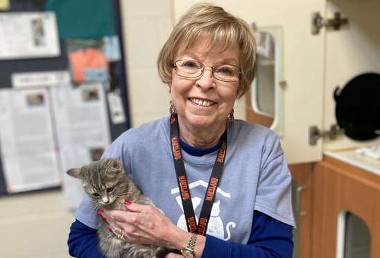 Portrait of Judith (Judy) Brocksmith '64 with a soft focus at an animal shelter. Judy gently holds a small tabby cat while smiling for the camera